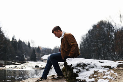 Side view of young man looking at frozen lake against sky