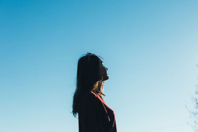 Side view of young woman standing against clear blue sky
