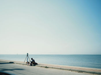 Full length of man sitting against sea and sky