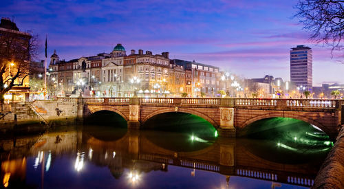 Arch bridge over river by buildings in city at night