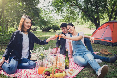 Women toasting juice glasses with while sitting with friend on field