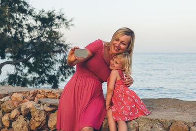 Portrait of happy mother with daughter against sky