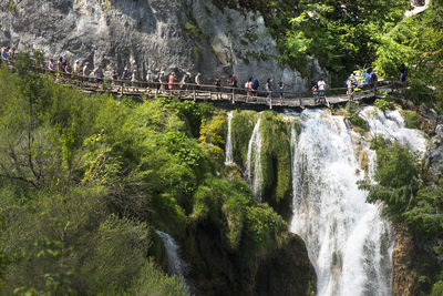 People walking on footbridge by waterfall