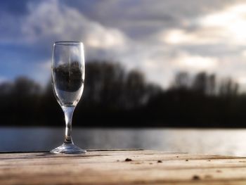 Close-up of glass on table against lake during sunset