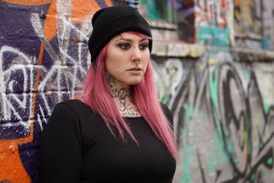 Young woman with pink hair standing against graffiti wall