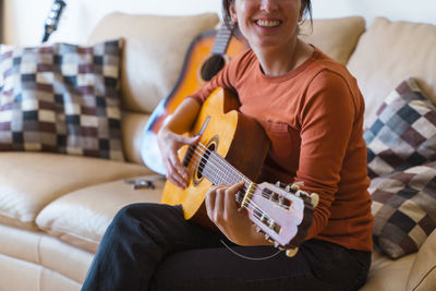 Woman playing guitar on sofa at home