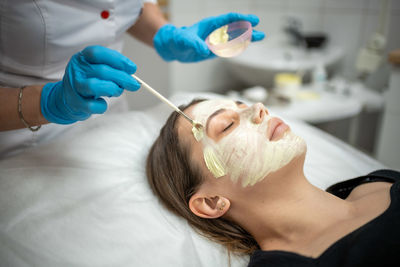 Beautician applying face mask to customer at spa