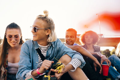 Happy friends sitting against clear sky at event during sunny day