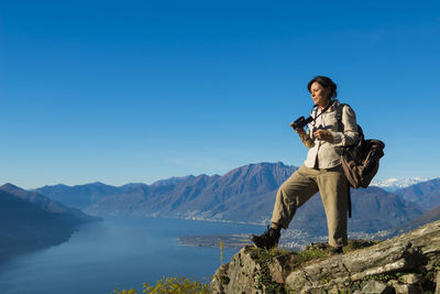 Female hiker photographing on cliff against swiss alps