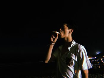 Young man smoking against black background