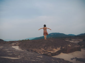 Rear view of girl standing on rock against sky