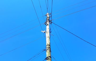 Low angle view of electricity pylon against blue sky