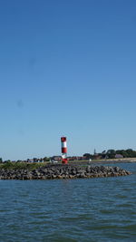 Lighthouse by sea against clear sky