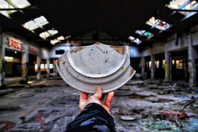 Cropped hand of person holding broken plate in abandoned building