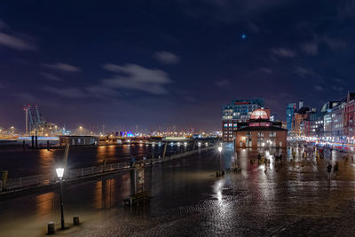 Illuminated city by river against sky at night