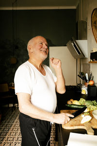 Happy senior man chopping fruits in kitchen at home