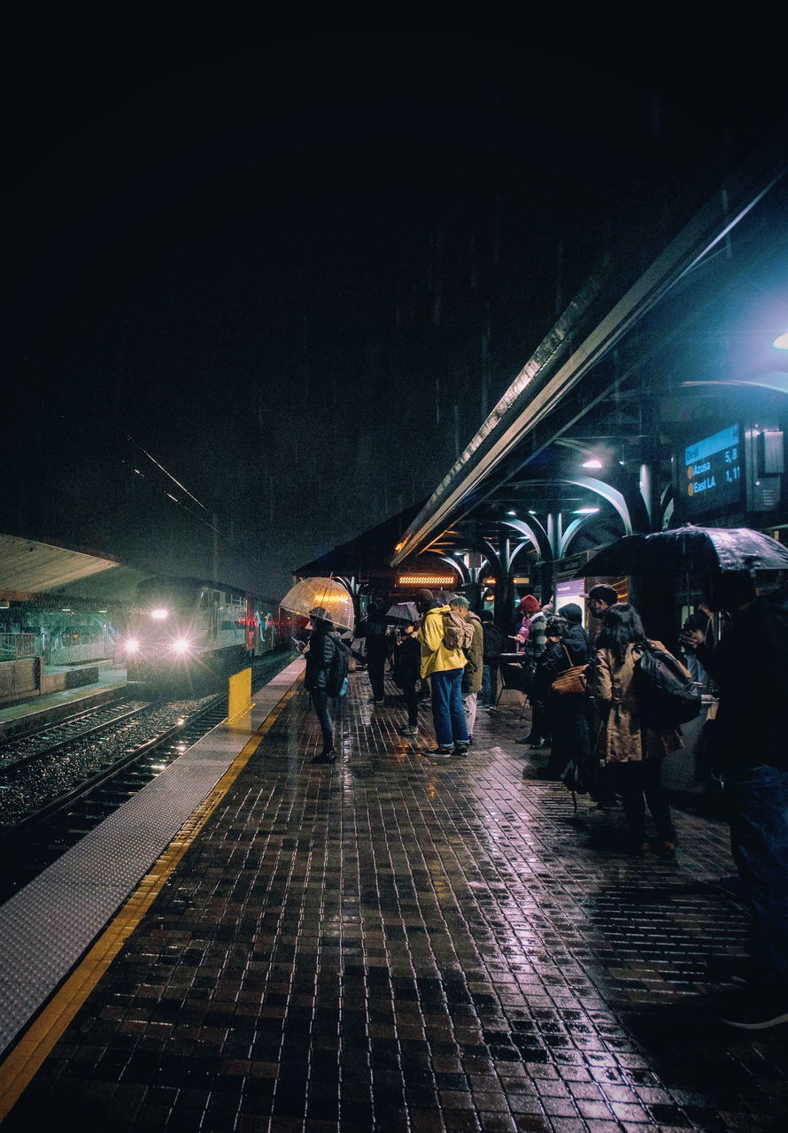 night, transportation, illuminated, rail transportation, public transportation, large group of people, real people, train - vehicle, men, railroad station platform, women, mode of transport, railroad track, travel, lifestyles, outdoors, full length, sky, adult, people