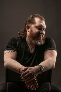 Young man looking away while sitting against black background