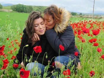 Mother kissing daughter amidst poppies on field