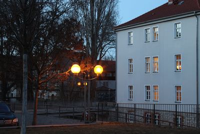 Illuminated street by building against sky at night