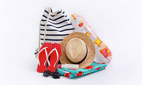 Close-up of hat and slippers with inflatable ring by bag over white background