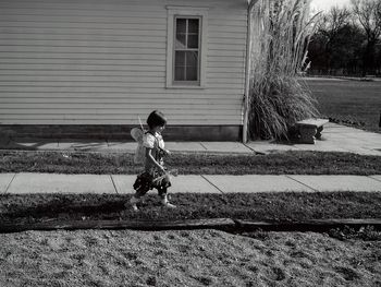 Side view of girl wearing costume wing against house in back yard