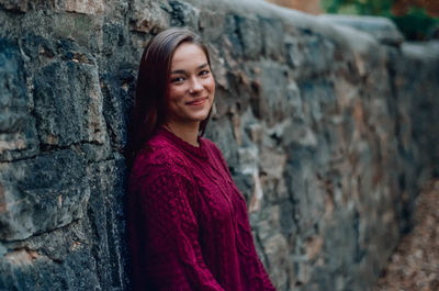 Portrait of smiling young woman standing by wall outdoors