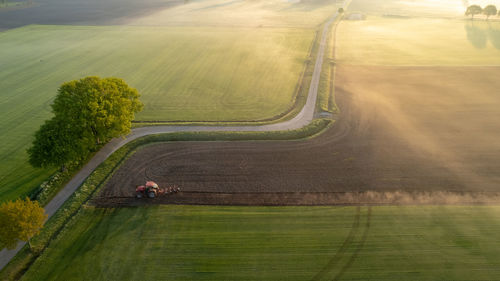 Aerial drone view of a tractor plowing field in the early morning fog lit up the golden sunrise.