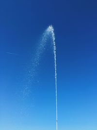 Low angle view of water spraying against clear blue sky