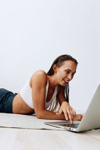Young woman using laptop while sitting on table against white background