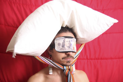 Man with pillow tied on head while wearing paper currency sleep mask