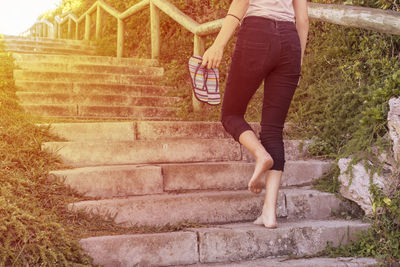 Low section of girl holding flip-flops while climbing staircase