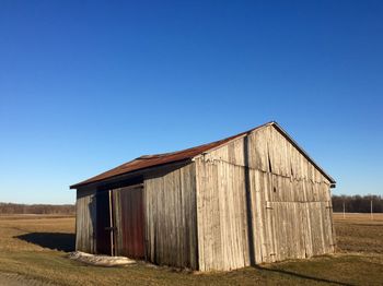 Barn on field against clear blue sky