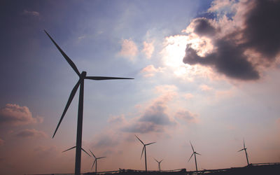 Low angle view of wind turbines on field against sky