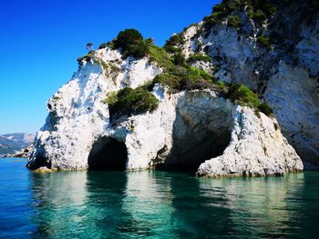 Rock formations in sea against clear blue sky