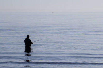 Silhouette man fishing in sea against sky