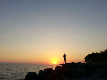 Silhouette woman standing on rock by sea against clear sky during sunset