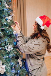 Beautiful young woman in santas hat decorating christmas tree. new year decoration. home interior.