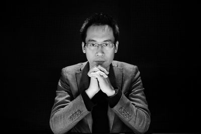 Portrait of young man with hands clasped against black background