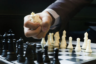 Midsection of person holding chess pieces over board