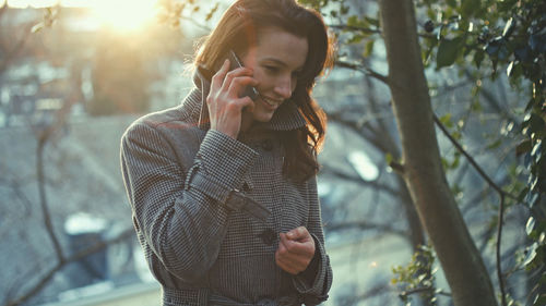 Young woman talking on mobile phone against tree