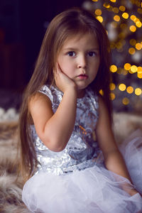 Baby girl sitting in studio in dress with christmas tree in christmas with long hair