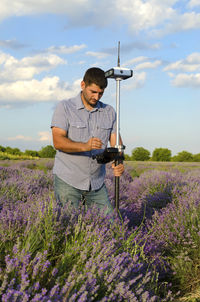 Surveyor using equipment on lavender field against cloudy sky