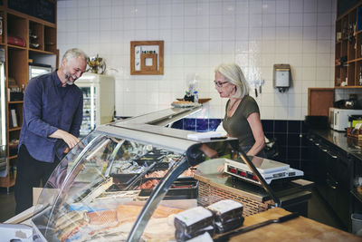 Customer smiling while showing seafood at retail display to saleswoman in deli