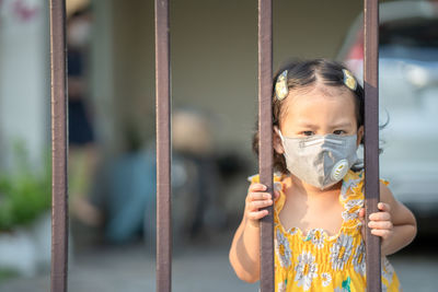 Girl standing at fence wearing medical face mask to prevent flu, pollution and covid 19.