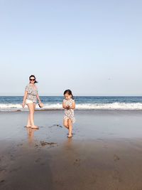 Mother and daughter walking at beach against clear sky