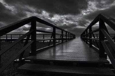 Footbridge over pier against sky at dusk