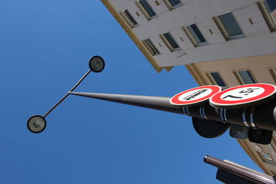 Low angle view of road signs on street light against clear blue sky