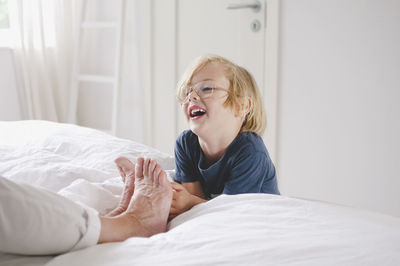 Happy grandson tickling grandmother's bare feet on bed at home