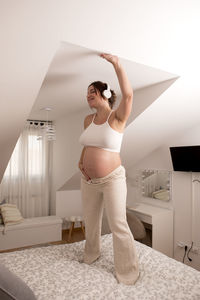 Beautiful pregnant woman, dancing and listening to music on the bed